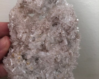 Puede incluir: Un cúmulo de cristales de cuarzo transparentes con un tono rosado. Los cristales están dispuestos en un patrón aleatorio y orgánico, creando una exhibición única y hermosa.