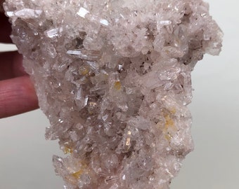 Puede incluir: Un cúmulo de cristales de cuarzo transparentes con un tono rosado y algunas inclusiones amarillas. Los cristales están dispuestos en un patrón aleatorio y orgánico.