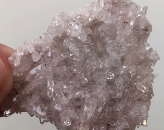 Puede incluir: Un cúmulo de cristales de cuarzo transparentes con un tono rosado. Los cristales están dispuestos en un patrón aleatorio y tienen una textura rugosa y natural.