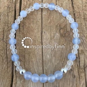 May include: A light blue and clear glass beaded bracelet with a silver bead accent. The bracelet is on a wooden surface.