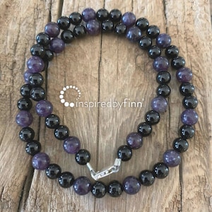 May include: A black and purple beaded necklace with a silver clasp. The necklace is made of round beads and is approximately 18 inches long.