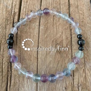 May include: A bracelet made of clear, green, purple, and black beads. The bracelet is made of fluorite and black onyx beads.