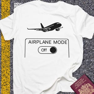 May include: White t-shirt with a black graphic of an airplane above a rectangle with the words "AIRPLANE MODE" and an "Off" switch. The shirt is made of a soft material.
