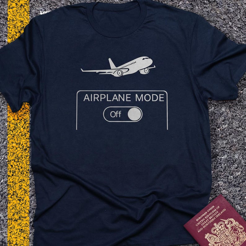May include: Navy blue t-shirt with a white airplane graphic and the text "AIRPLANE MODE Off". The design features an airplane icon above a toggle switch, suggesting a travel or tech theme.