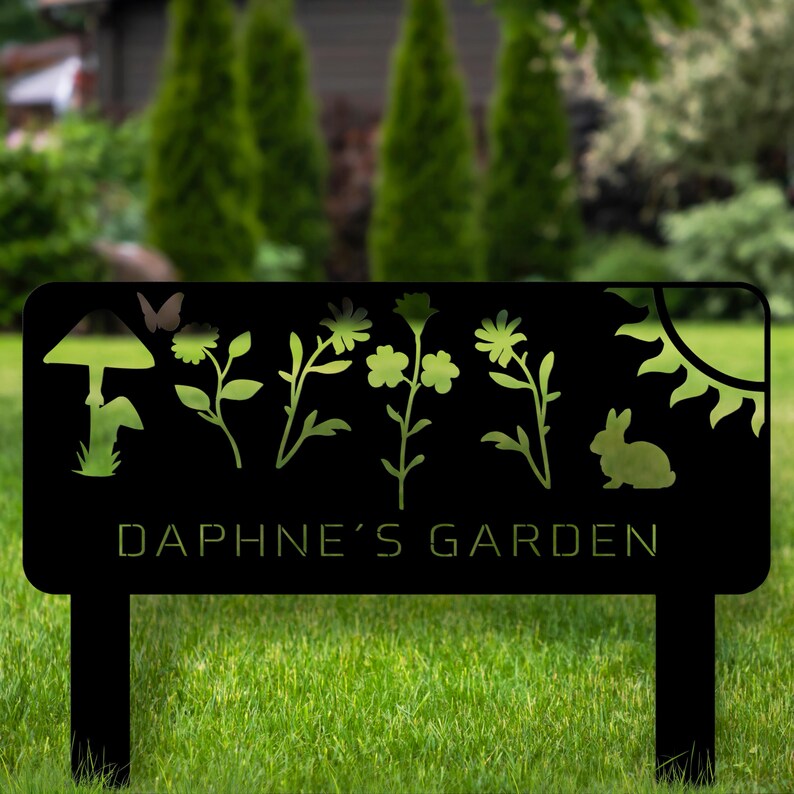 Puede incluir: Letrero de jard&iacute;n de metal negro con dise&ntilde;os recortados de una seta, una mariposa, flores, un sol y un conejo. El letrero dice "DAPHNE'S GARDEN". El letrero tiene dos estacas para colocarlo f&aacute;cilmente en un jard&iacute;n.
