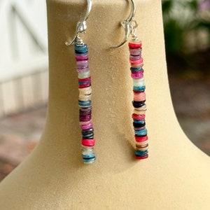 May include: A pair of dangle earrings with a silver hook and a long strand of colorful, round, flat beads. The beads are in shades of pink, blue, purple, and white.