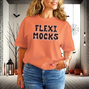May include: A woman wearing an orange t-shirt with the text "Flexi Mocks" in black dripping letters. The shirt is a relaxed fit and has short sleeves.