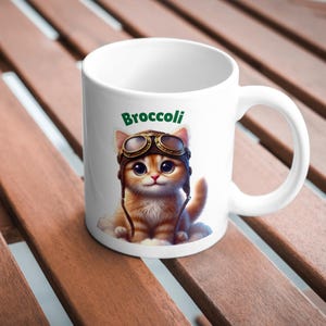 May include: White ceramic mug with a cartoon illustration of a cat wearing goggles and a pilot's hat. The text "Broccoli" is printed in green above the cat.