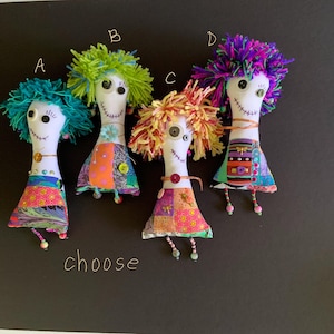 May include: Four handmade fabric dolls with yarn hair in teal, green, yellow, and purple. Each doll has button eyes, stitched smiles, and patchwork dresses. The word "choose" is written below the dolls.