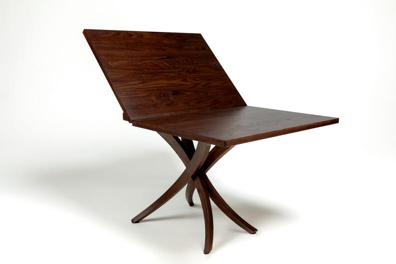 May include: A dark brown wooden table with a unique X-shaped base. The table top is rectangular and has a leaf that can be raised to extend the table's length.
