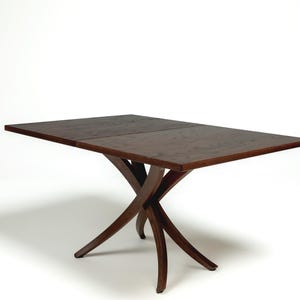 May include: A dark brown wooden dining table with a rectangular top and a unique, curved, X-shaped base.