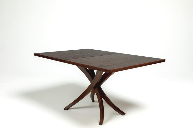 May include: A dark brown wooden dining table with a rectangular top and a unique, curved, X-shaped base.