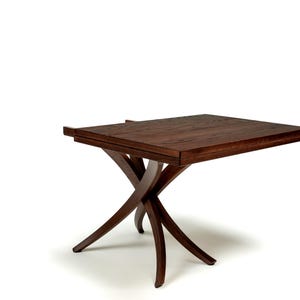 May include: A dark brown wooden table with a rectangular top and an X-shaped base. The table is made of solid wood and has a natural finish.