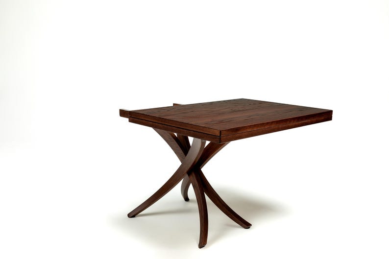 May include: A dark brown wooden table with a rectangular top and an X-shaped base. The table is made of solid wood and has a natural finish.