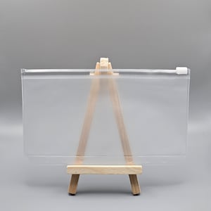 May include: A clear, rectangular zippered pouch with a white zip, displayed on a small wooden easel. The pouch is made of a translucent material, ideal for storing items. The easel has a natural wood finish.