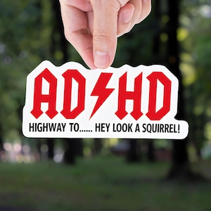 Funny ADHD sticker with bold red and black text that says “ADHD Highway to… Hey look a squirrel!” in a rock-band inspired design.