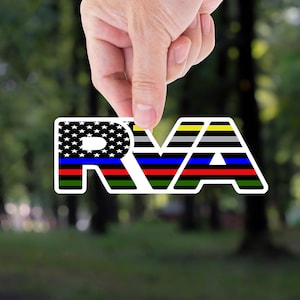 May include: A white sticker with the letters "RVA" in a bold, stylized font. The "R" features a design of the American flag, while the "V" and "A" have stripes in various colors, including blue, red, and yellow. The sticker is held up by a hand.