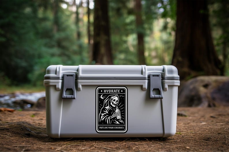 May include: A gray, rectangular cooler with a black and white sticker featuring a Grim Reaper holding a water bottle. The sticker reads "HYDRATE" and "OUTLIVE YOUR ENEMIES". The cooler is outdoors.