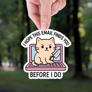May include: A sticker featuring a cartoon cat holding a knife, sitting inside a pink laptop. The text on the sticker reads "I HOPE THIS EMAIL FINDS YOU BEFORE I DO". The background is a blurred forest.