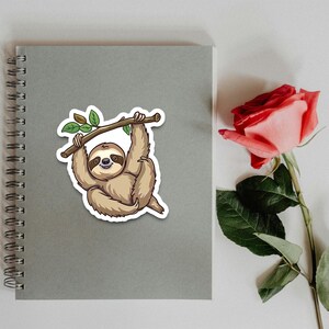 May include: A cartoon sloth hanging from a branch with green leaves. The sloth is brown and has a happy expression on its face.