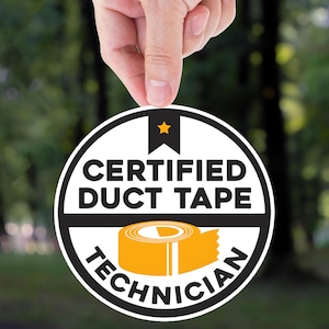 May include: A round, black and white sticker with the words "CERTIFIED DUCT TAPE TECHNICIAN" encircling a yellow roll of duct tape. A small gold star is at the top. The sticker is held by a hand against a blurred green background.