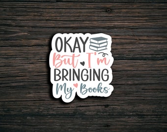 May include: White sticker with the text "Okay But I'm Bringing My Books" in gray and pink lettering. A stack of three books is above the text.