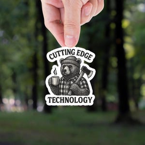 May include: A black and white illustration of a bear wearing a plaid shirt and a hat, holding a cup of coffee and an axe. The text "Cutting Edge Technology" is above the bear and the text is in a black font.