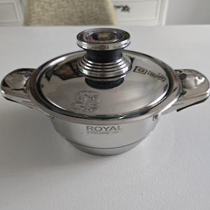 Puede incluir: Una olla de cocina de acero inoxidable con tapa y dos asas laterales. La olla tiene las palabras "ROYAL EXCLUSIVE LINE" impresas en el lateral. La tapa tiene un asa negra con la parte superior plateada.