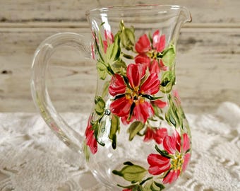 May include: A clear glass jug with a handle, hand-painted with pink flowers and green leaves.
