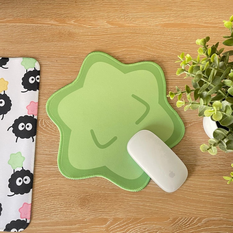 May include: A green star-shaped mousepad with a cartoon face on it. A white wireless mouse is on top of the mousepad.