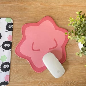 May include: A pink star-shaped mousepad with a white mouse on top. The mousepad has a cartoon-like face with closed eyes and a small mouth.