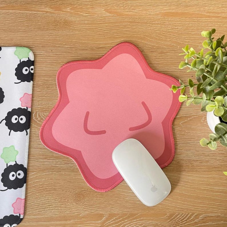 May include: A pink star-shaped mousepad with a white mouse on top. The mousepad has a cartoon-like face with closed eyes and a small mouth.