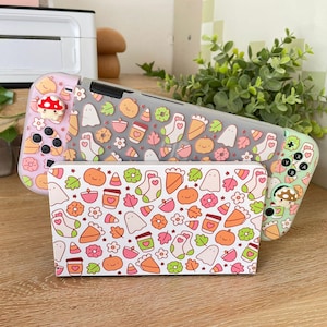 May include: Two Nintendo Switch cases with a fall-themed design. The cases are pink and green with a white background and feature various fall-themed icons such as ghosts, pumpkins, leaves, and coffee cups.