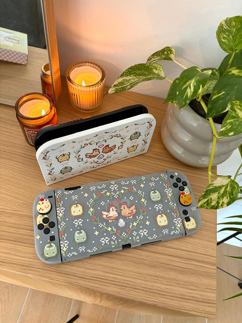 May include: A gray Nintendo Switch case and controller with a pixelated design featuring birds, flowers, and other small icons. The case and controller have a matching design. The controller buttons have decorative chicken-shaped toppers.