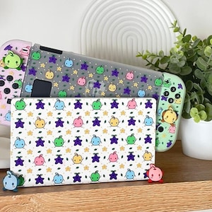 Op de afbeelding: Twee Nintendo Switch-gameconsole-hoesjes met een fruit- en sterpatroon. De hoesjes zijn roze, groen en grijs met een witte achtergrond. De hoesjes zijn versierd met kleine cartoonachtige fruit- en sterontwerpen.