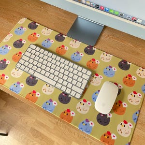 May include: A yellow desk mat with a repeating pattern of colorful cartoon chickens. A white keyboard and a white mouse are on the mat.