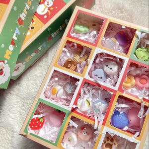 以下が含まれることがあります： 複数のコンパートメントを持つカラフルなギフトボックス。それぞれに異なる装飾品が入っています。イチゴ、雲、クマ、花など。ボックスは赤、緑、黄色の色で装飾されています。