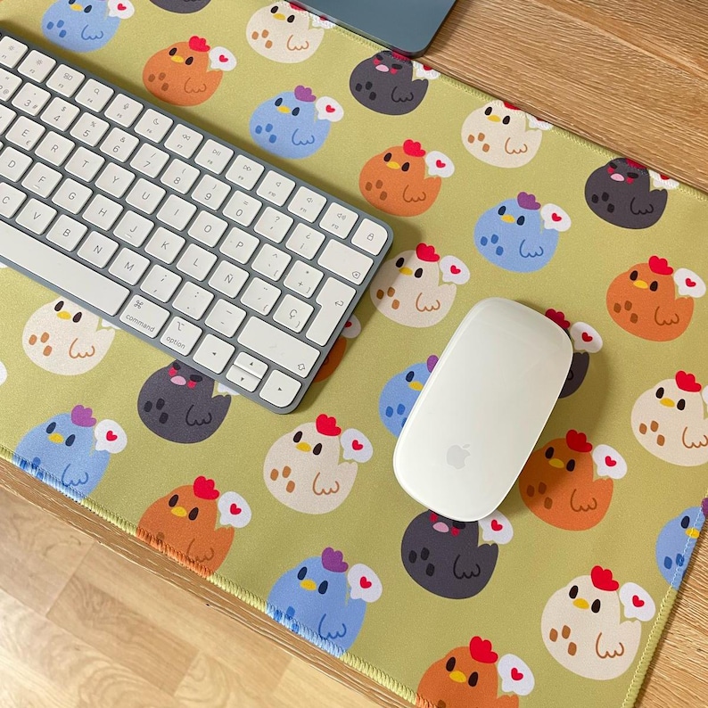 May include: A green mousepad with a repeating pattern of cartoon chicks and eggs. The mousepad has a white keyboard and a white wireless mouse on top of it.