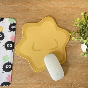 May include: A yellow star-shaped mousepad with a white computer mouse on top. The mousepad has a slightly raised edge.