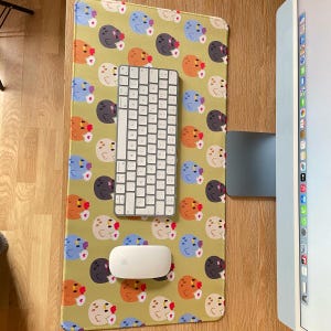 May include: A green desk mat with a repeating pattern of colorful cartoon chickens. A white wireless keyboard and mouse are on the mat.