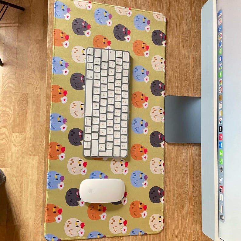 May include: A green desk mat with a repeating pattern of colorful cartoon chickens. A white wireless keyboard and mouse are on the mat.