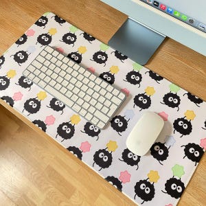May include: A white desk mat with a repeating pattern of black fluffy creatures holding yellow stars. A white keyboard and a white mouse are on the mat.