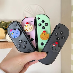 May include: Four Nintendo Switch controllers with different colored cases. Each controller has a small, colorful chicken-shaped button cap.