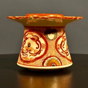 May include: A small, white ceramic vase with a wide, scalloped rim. The vase is decorated with a red, orange, and white floral pattern.