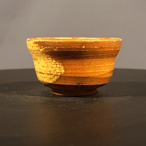 May include: A small, brown ceramic bowl with a yellow glaze. The bowl has a rounded shape and a slightly flared rim.