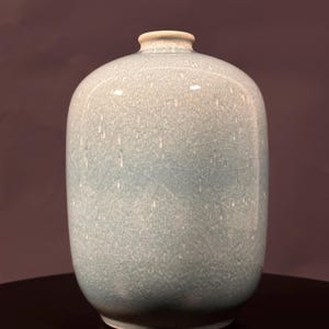May include: A celadon-glazed ceramic vase with a crackle finish. The vase has a rounded body and a narrow neck. The color is a pale blue-green, and the surface has a network of fine cracks. The vase is likely of Asian origin.