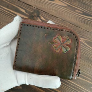 Cartera con cremallera de piel auténtica. En la parte frontal luce un "Trébol" grabado.