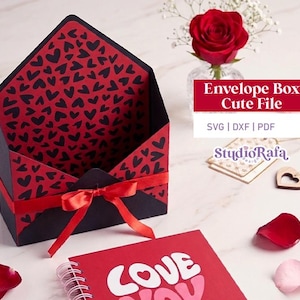 Pode incluir: Uma caixa de envelope preta e vermelha com um padrão de coração, amarrada com uma fita vermelha. A caixa está aberta, revelando o interior com padrão de coração. O texto "Envelope Box Cute File" é exibido em uma faixa vermelha. Um caderno vermelho com a palavra "LOVE" também é visível.