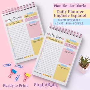 Może przedstawiać: Dwa spiralne plannery dzienne z sekcjami "My Day! To-Do List" i "Appointment". Planery mają różowe, żółte i niebieskie akcenty, z tekstem "Daily Planner English-Español" i "Ready to Print". Widoczne są również spinacze do papieru i mała roślina.