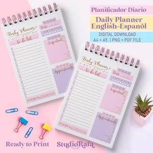 May include: Two spiral-bound daily planners with pink and lilac accents. Each planner has sections for to-do lists, dates, and appointments. The text "Daily Planner" and "to-do list" are visible. The image also includes paper clips and a small potted plant.